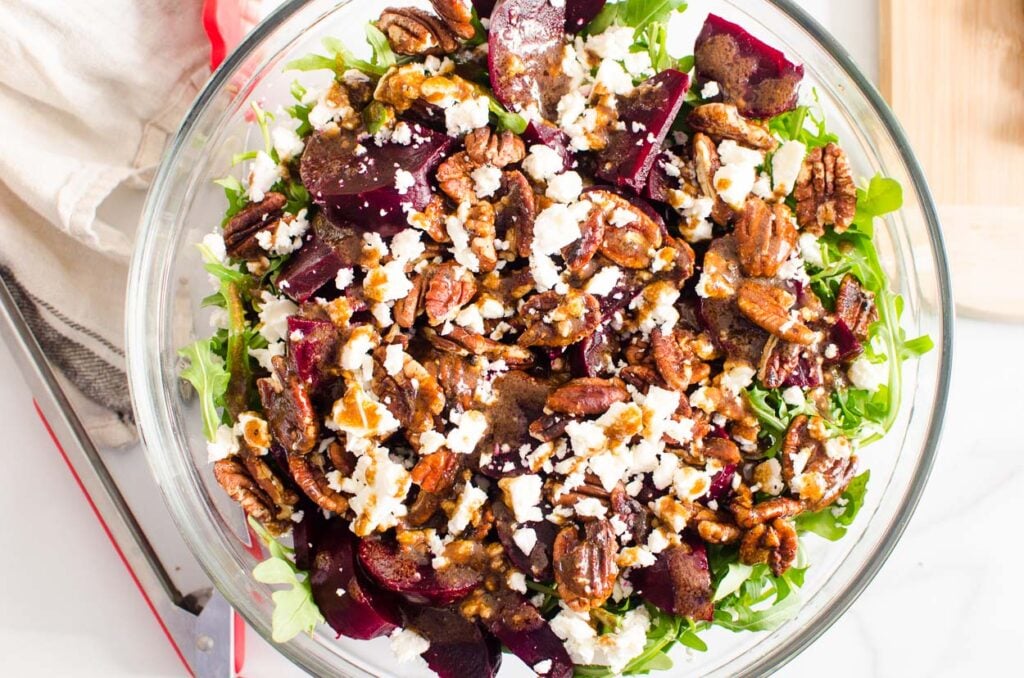 Arugula beet salad with feta cheese and pecans in glass bowl. 