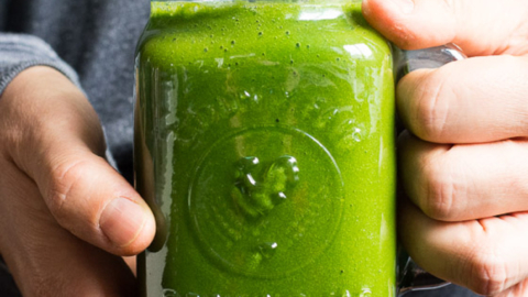 A person holding a jar with green smoothie and a straw.