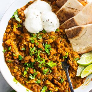 Green lentil curry with pita and sour cream in a bowl.