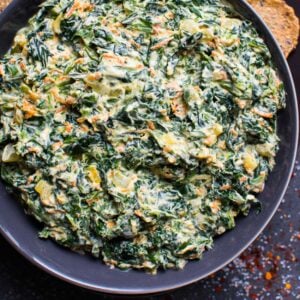 Healthy spinach dip in gray bowl with crackers nearby.