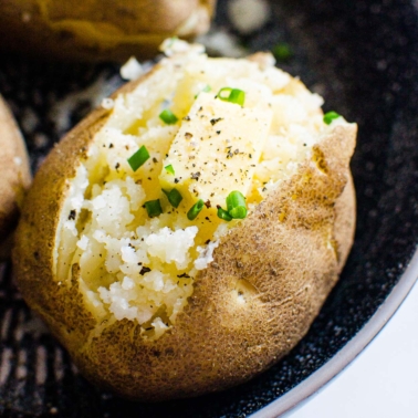 An Instant Pot baked potato split open with butter and chives.