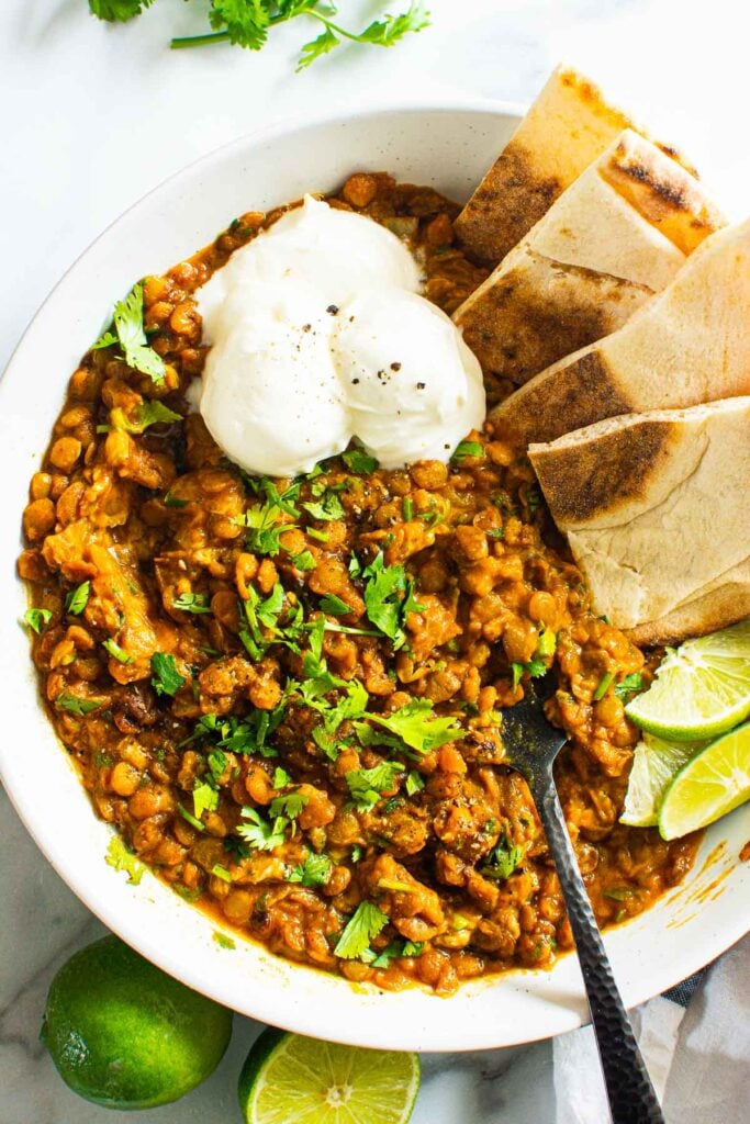 green lentil curry dish with lime garnish pita and sour cream
