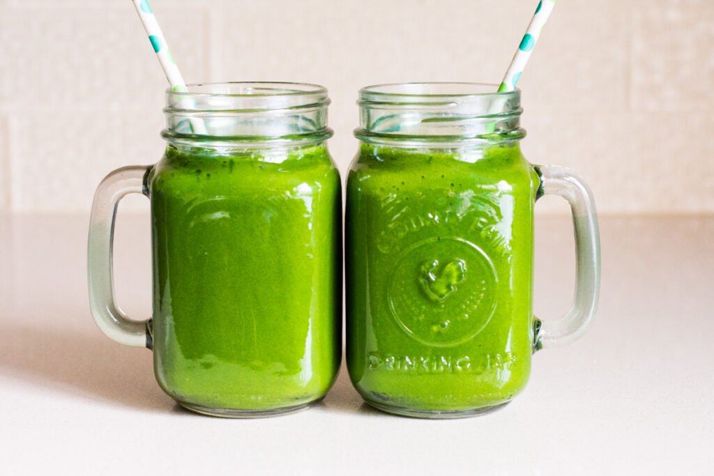 two green vegetable smoothies in glasses with straws