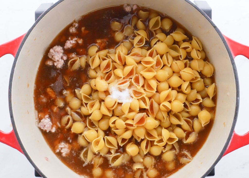 Small shell pasta in a pot with tomato sauce and ground turkey.
