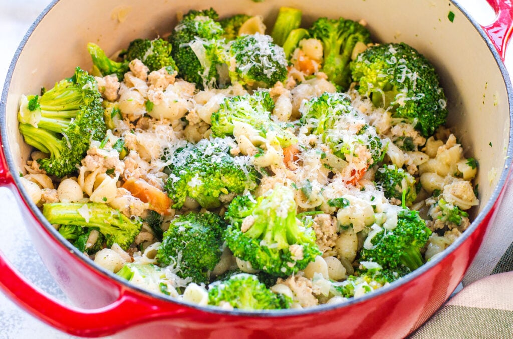 A red pot with melted cheese, broccoli, pasta, ground turkey and tomatoes.