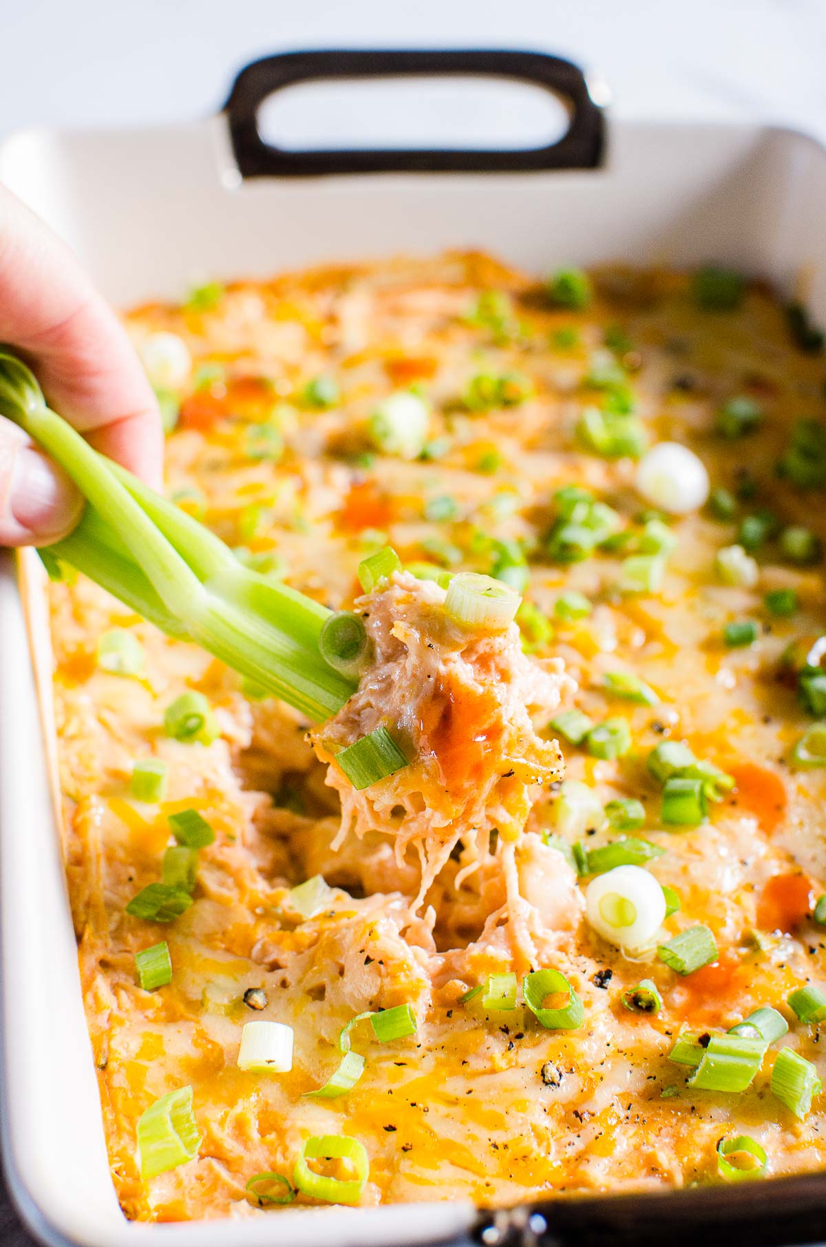 Healthy buffalo chicken dip in a dish with celery stick being dipped into it.