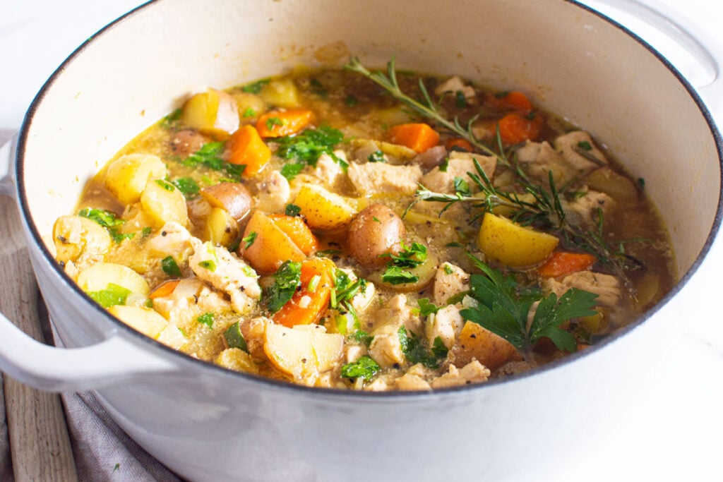 healthy chicken stew in a large stock pot garnished with fresh herbs