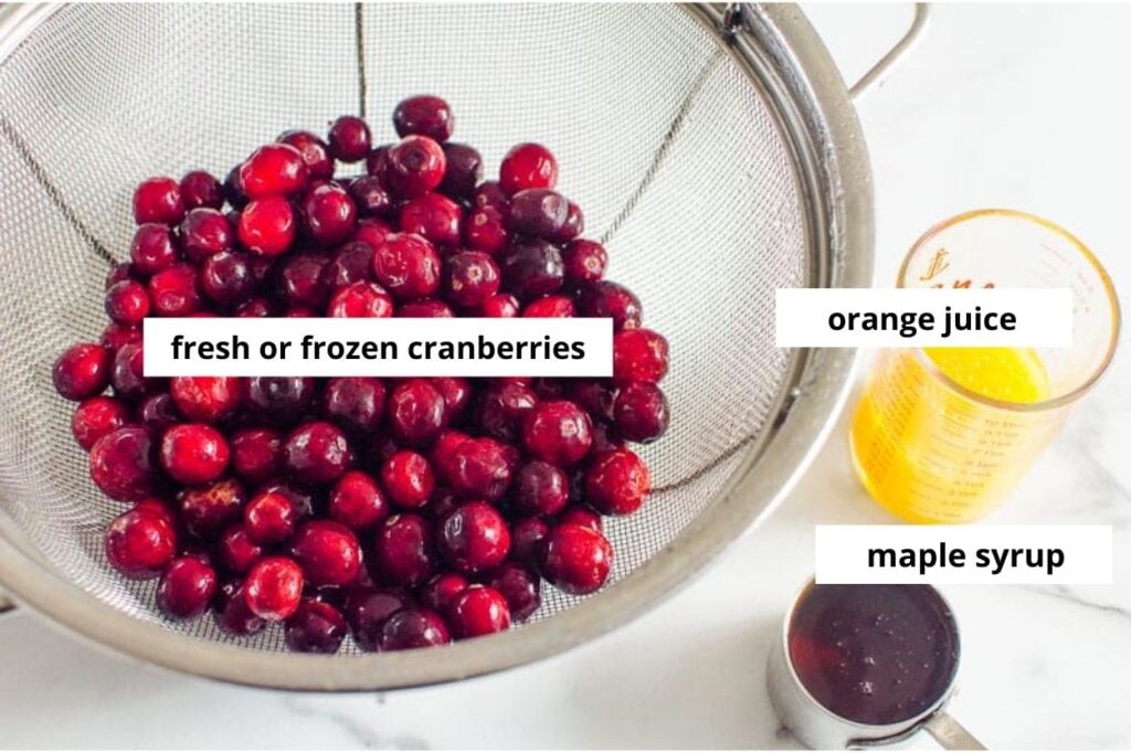 Cranberries in a colander, orange juice and maple syrup on kitchen counter.