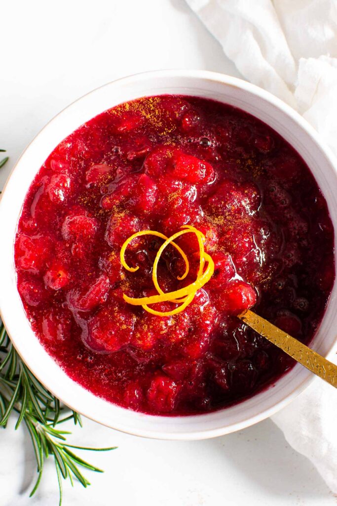 healthy cranberry sauce in white bowl with orange peels and rosemary