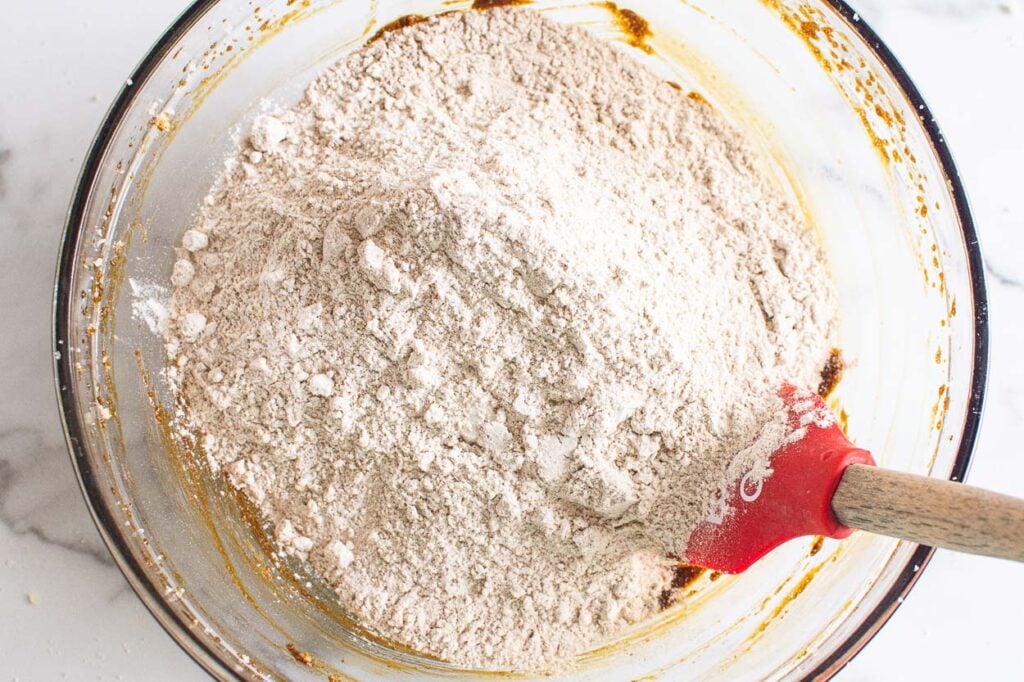 A bowl with red spatula and whole wheat and all purpose flour.