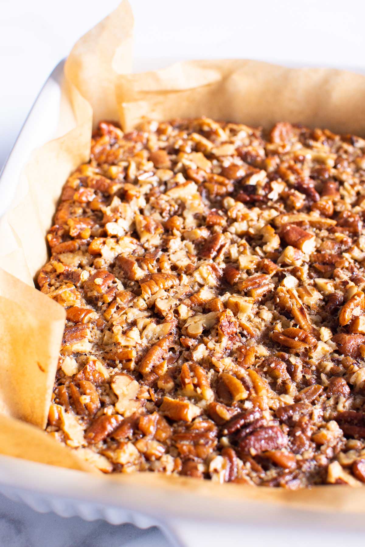 Close up of pecan pie bars in parchment lined pan.