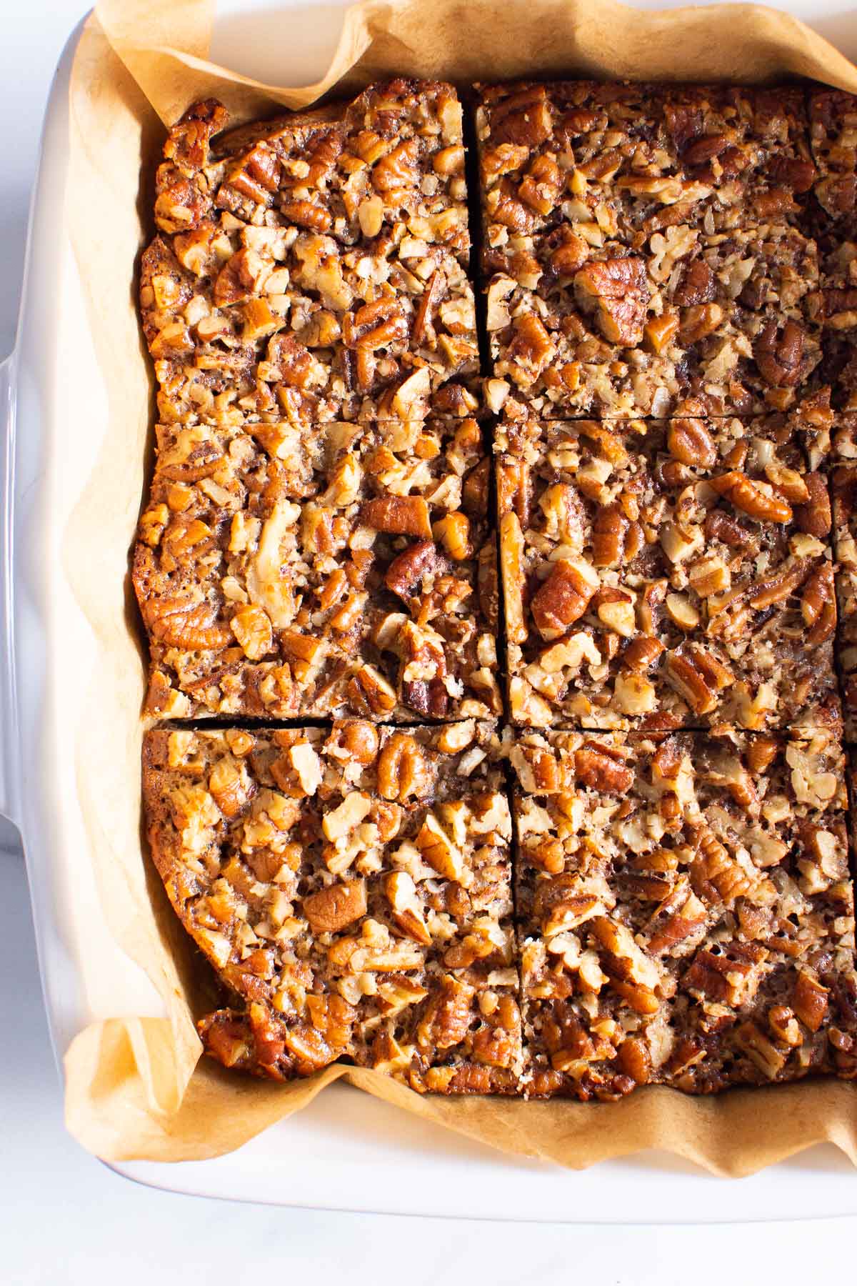 Pecan squares sliced in baking dish with parchment paper.