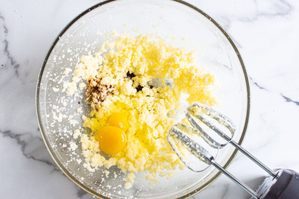 Eggs and vanilla mixed with sugar and butter in mixing bowl.