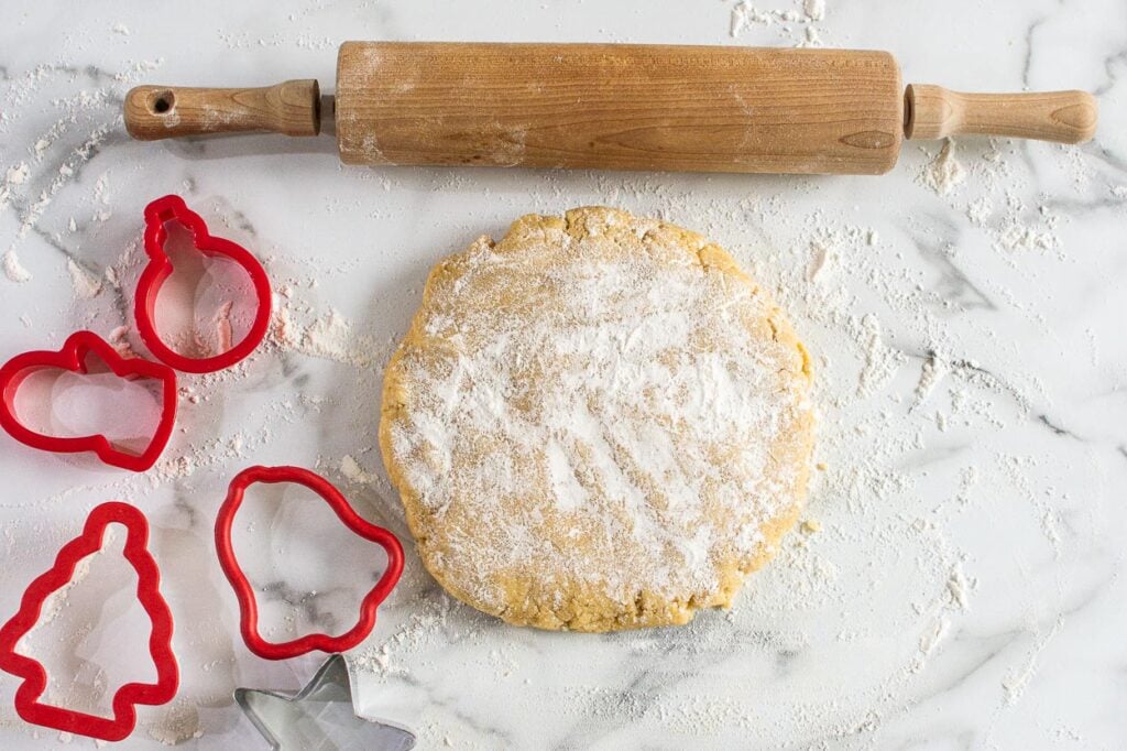 Dusting sugar cookie dough with flour, rolling pin and red cookie cutters.
