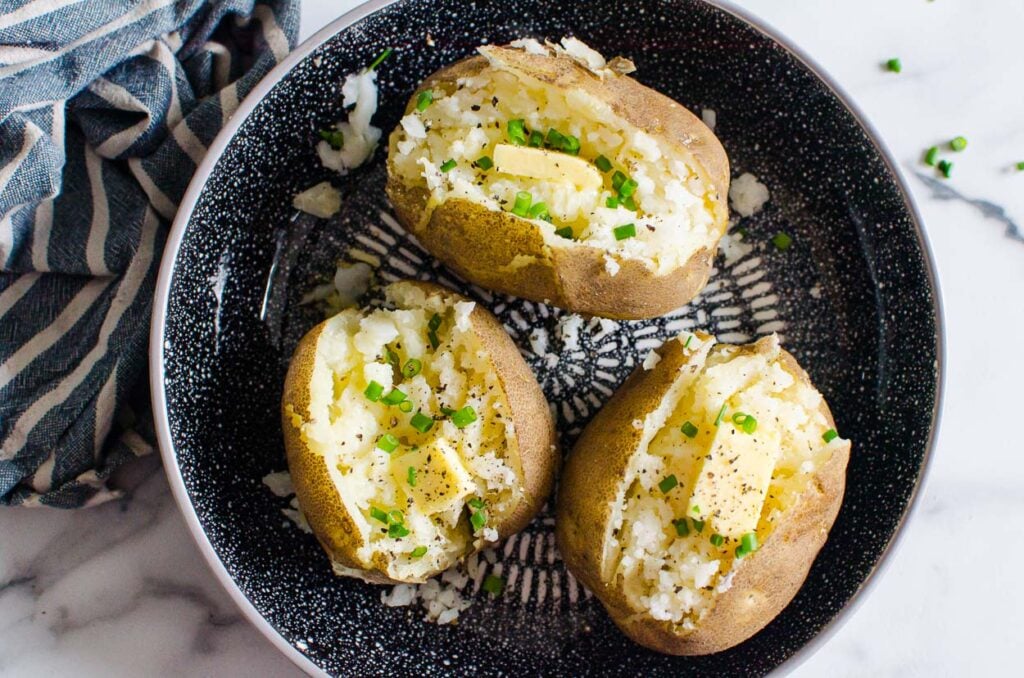 pressure cooker baked potatoes on plate with butter and chives ready to eat