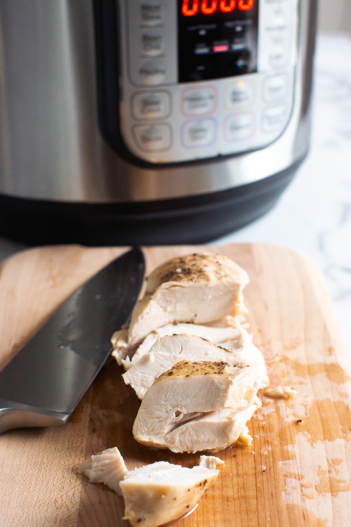Sliced chicken breast on a cutting board with Instant Pot in background.