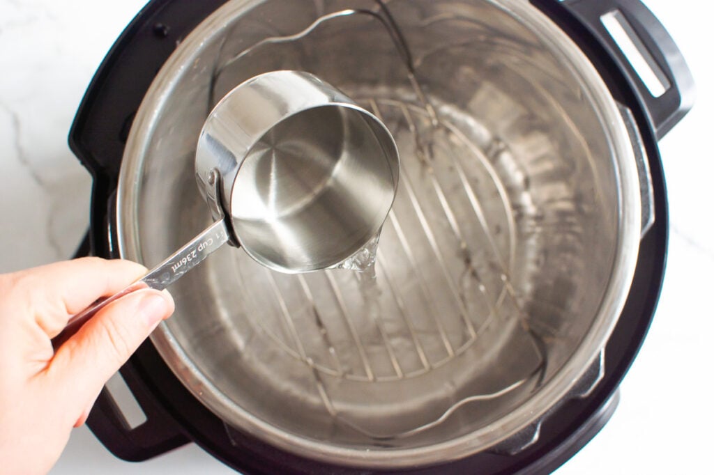 adding a cup of water to pressure cooker with trivet