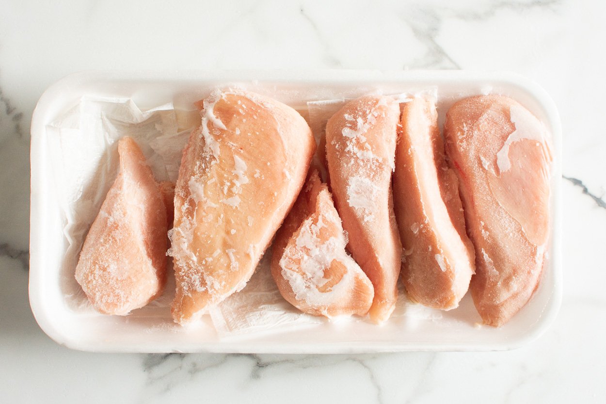 Six frozen chicken breasts on a tray.