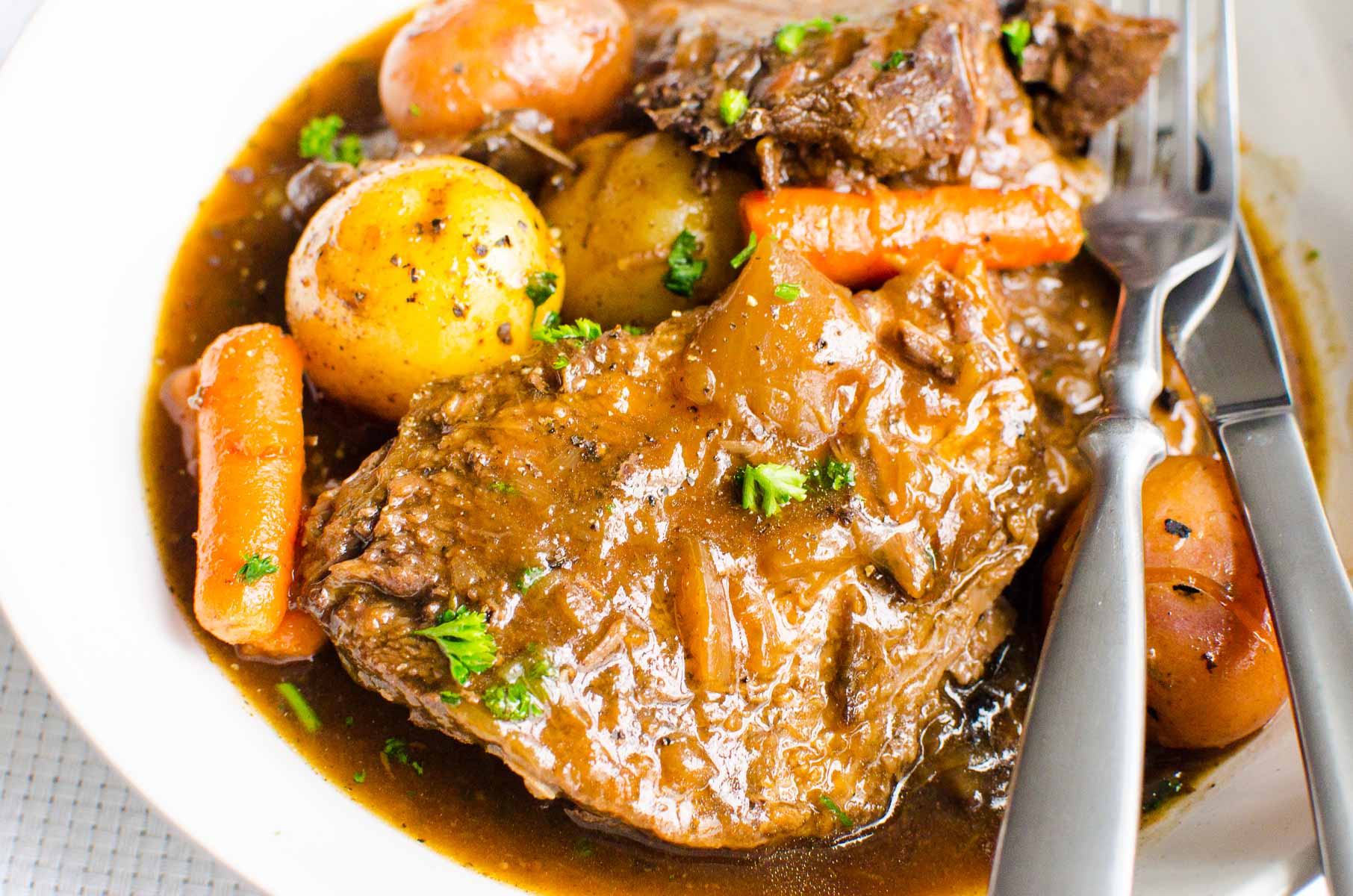 Instant Pot pot roast with carrots, potatoes and parsley on white plate with utensils.