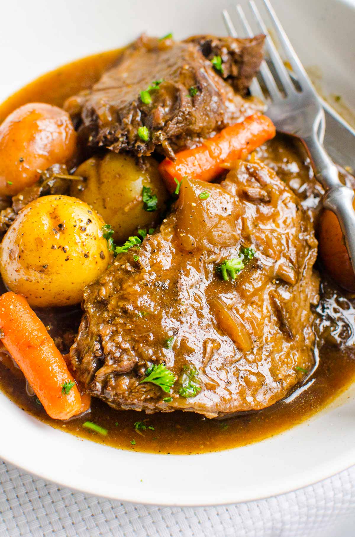 Instant Pot Pot Roast with potatoes and carrots in gravy with serving utensils.
