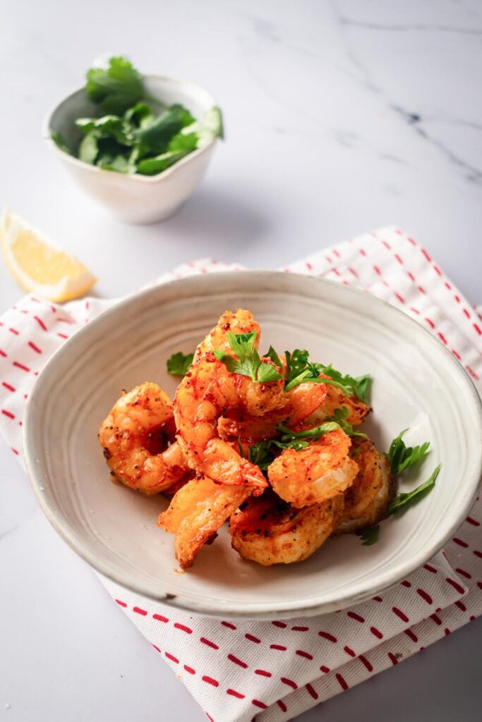 Air fryer shrimp in a deep white bowl with parsley and lemon slice.