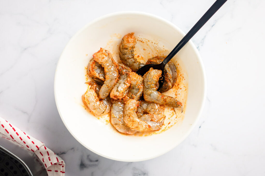 healthy air fryer shrimp being mixed in a bowl with seasonings