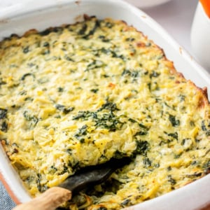 Healthy spinach artichoke dip in baking dish with a spoon.