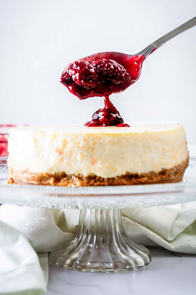 Spooning cherry compote onto a cheesecake.