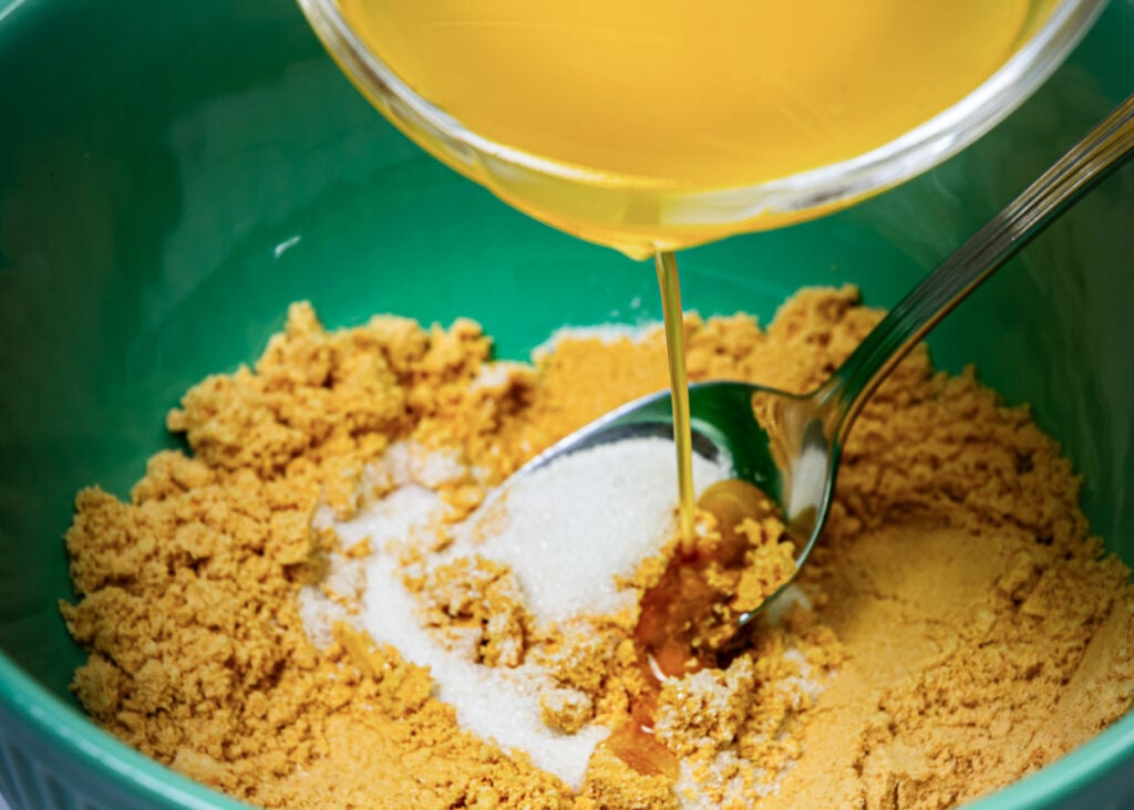 Melted butter being poured into bowl of graham cracker crumbs and sugar.