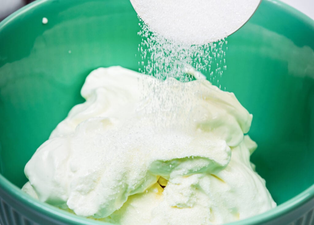 Adding sugar to cream cheese and Greek yogurt in a bowl.