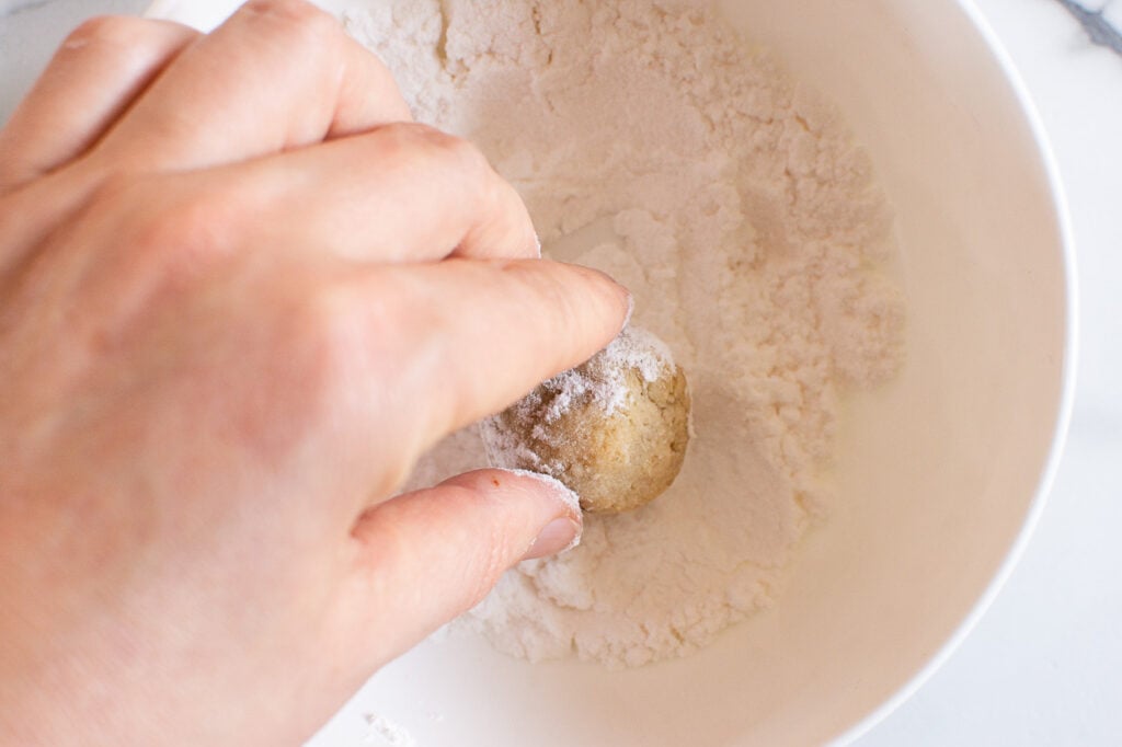 rolling almond flour mexican wedding cake in powdered sugar