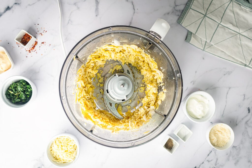 adding ingredients for artichoke dip to food processor