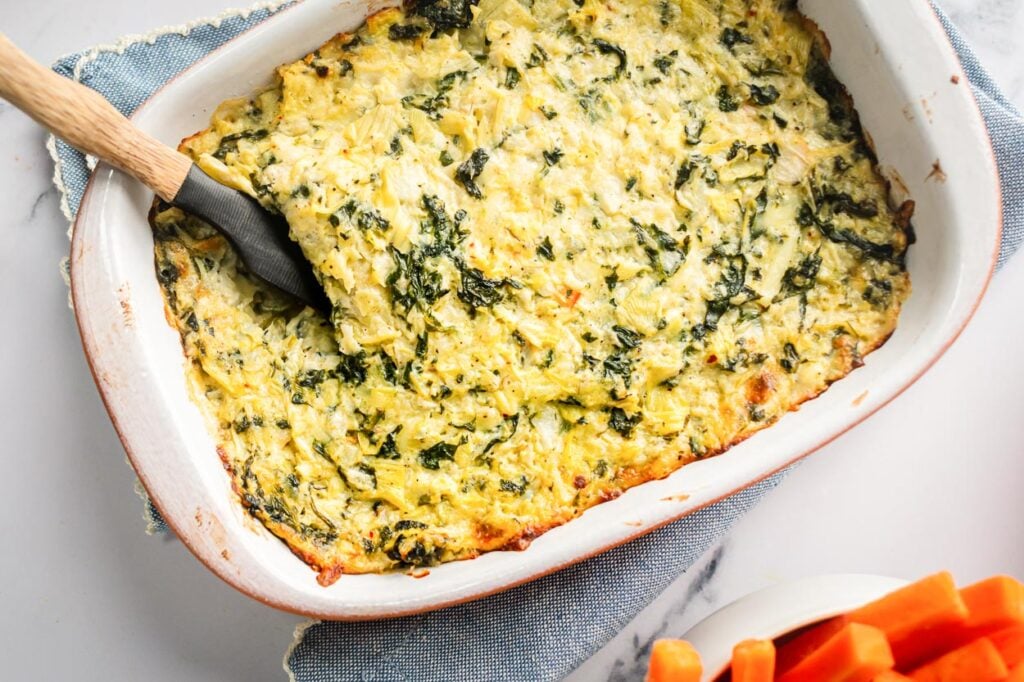 Baked healthy spinach artichoke dip with server in baking dish. 