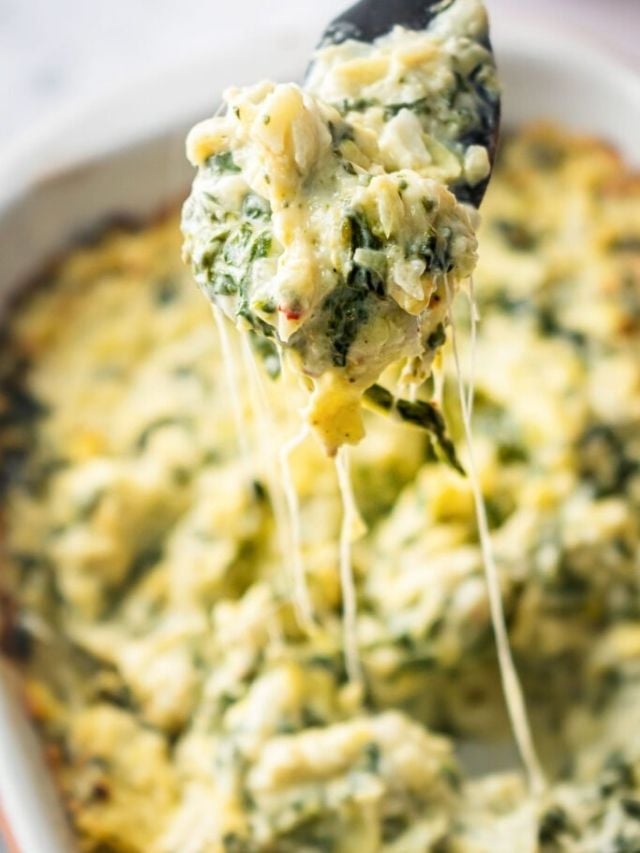 Healthy spinach artichoke dip dipped out of baking pan on spoon.