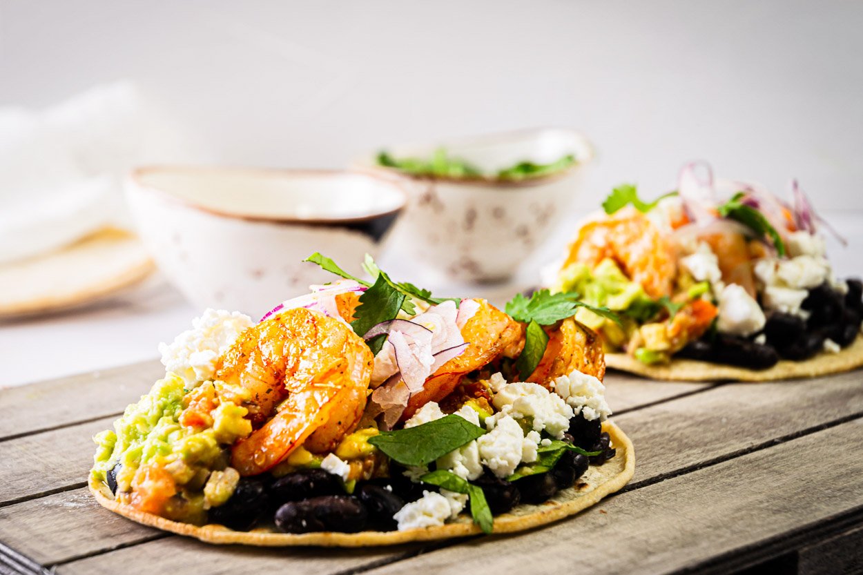 Two shrimp tostadas with toppings on a wooden board.