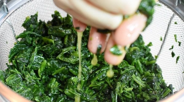 Squeezing water from spinach in colander. 