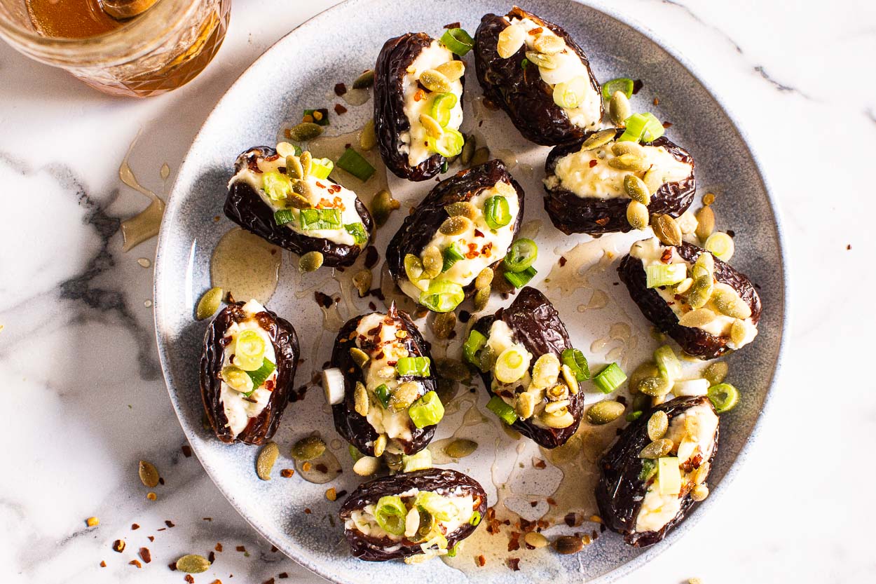 Stuffed dates on plate with green onion, pumpkin seeds and drizzled with honey.