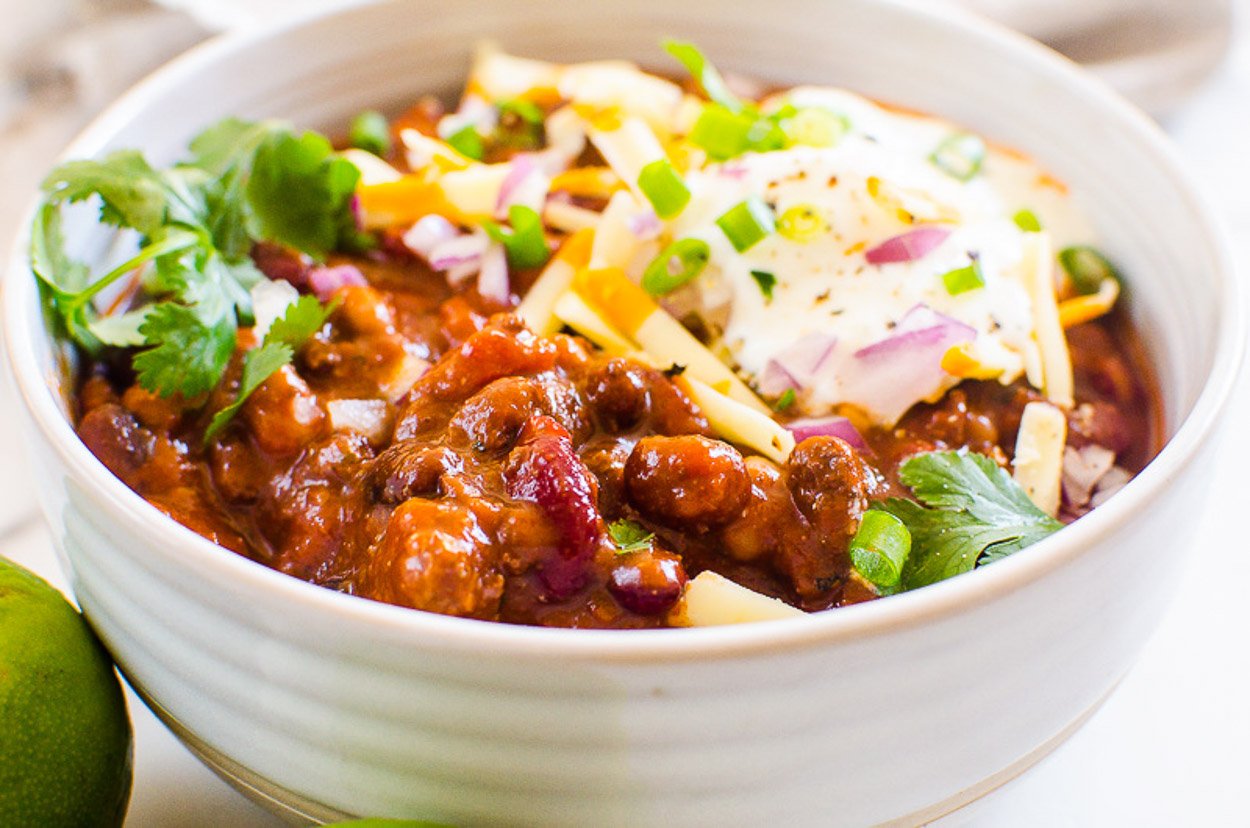 Chili with beans in white bowl topped with cheese, green onion and cilantro.