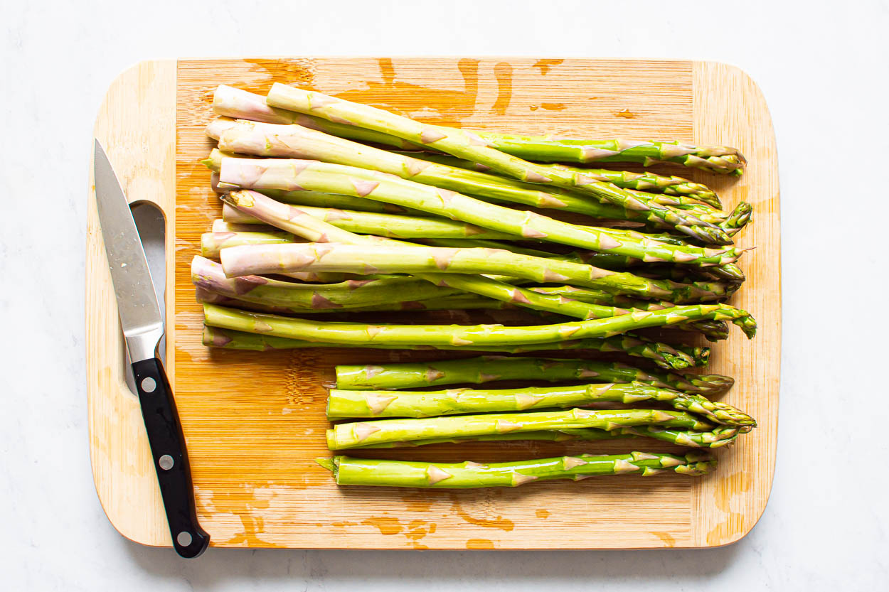Half trimmed asparagus and half not on cutting board with knife.