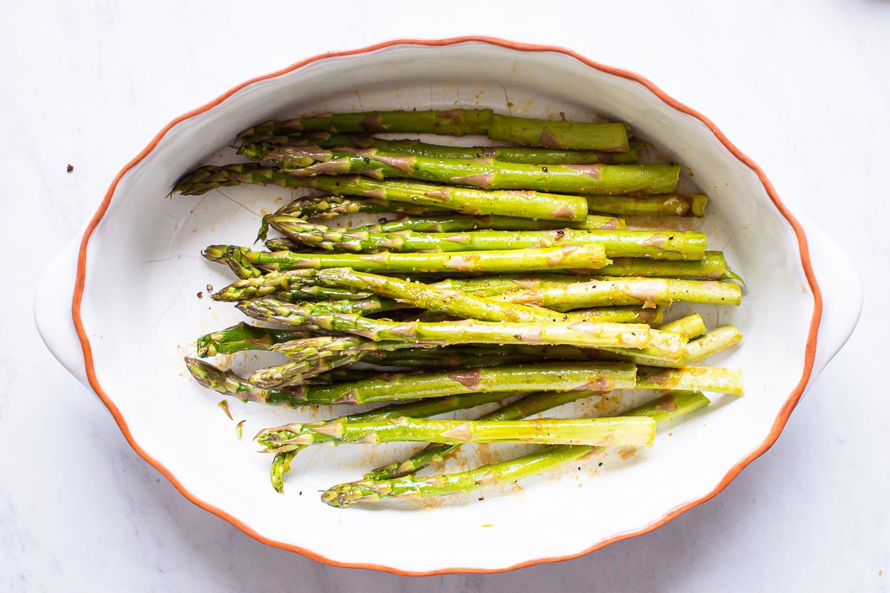Raw trimmed asparagus with seasonings in white dish.