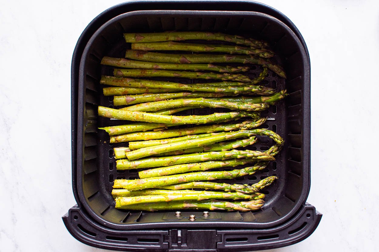 Uncooked seasoned asparagus in air fryer basket.