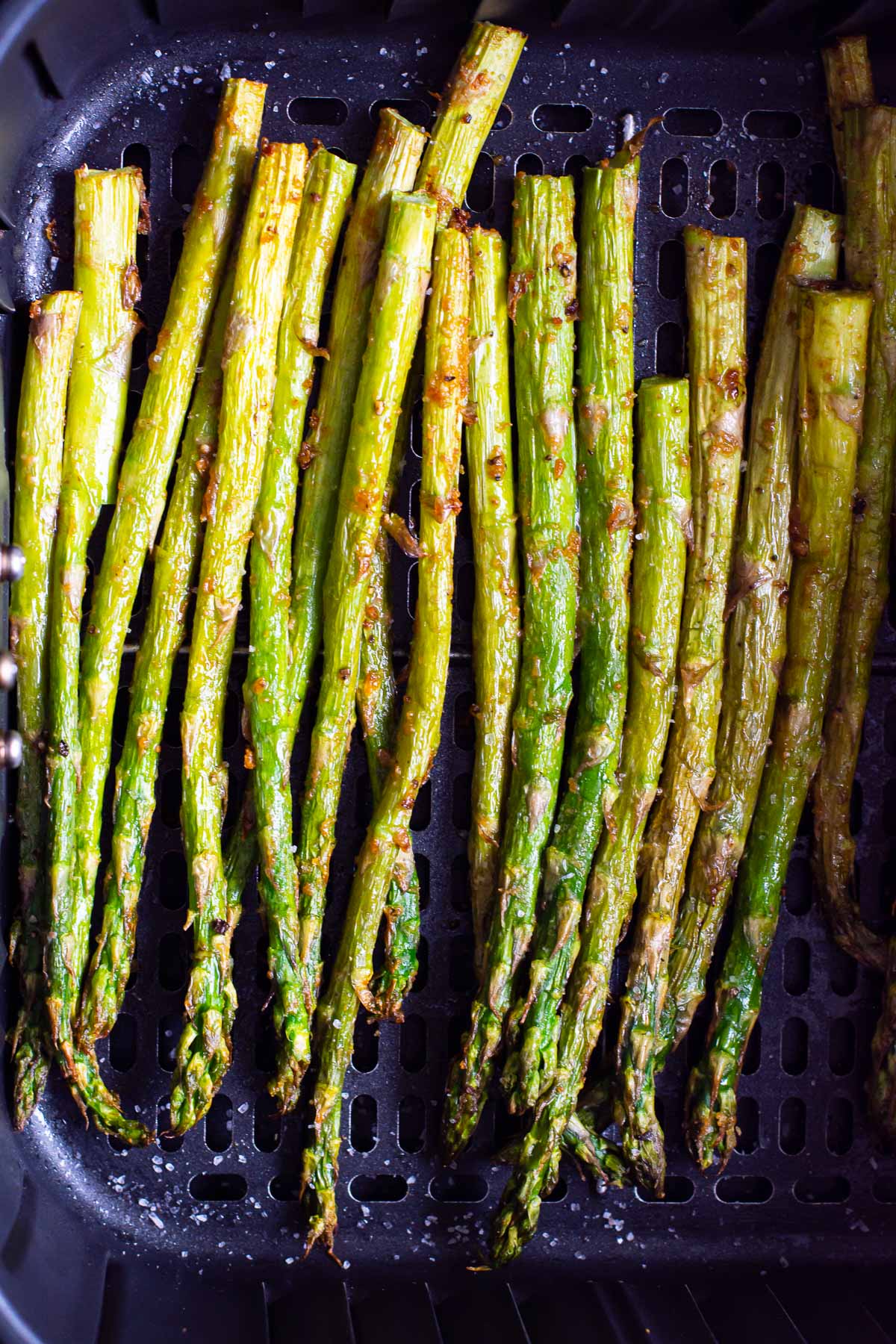 Air fryer asparagus in the air fryer basket with salt.