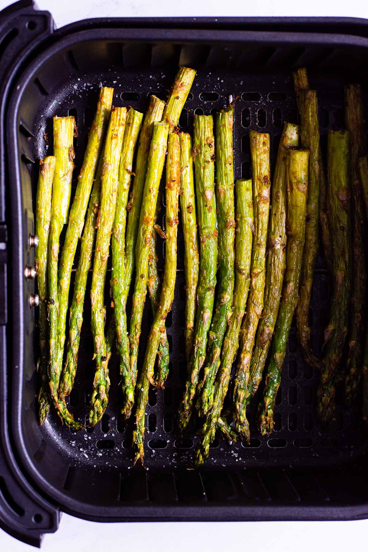 Cooked air fryer asparagus with golden brown bits and seasoned with salt.