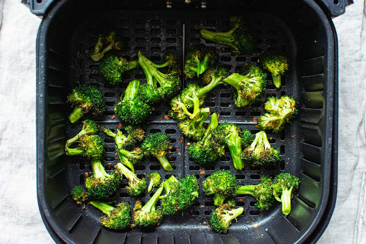 Broccoli in basket of air fryer with red pepper flakes.