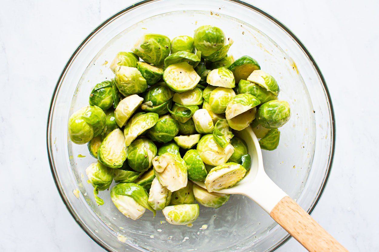 Mixing brussels sprouts with seasonings in glass bowl.