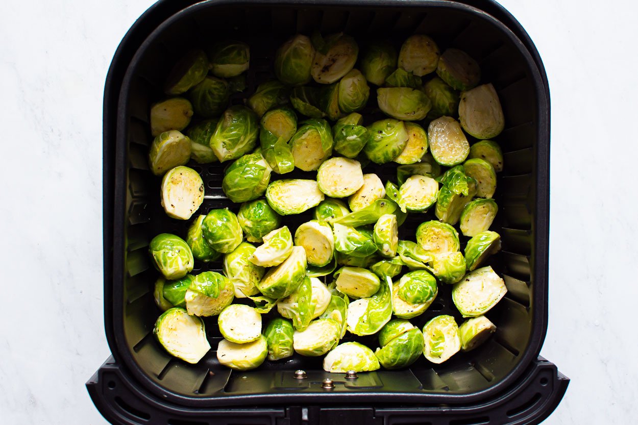 Seasoned uncooked brussels sprouts in air fryer in single layer.