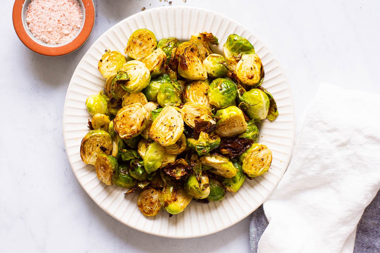 Air fried brussels sprouts on white plate and salt and linen towel nearby.