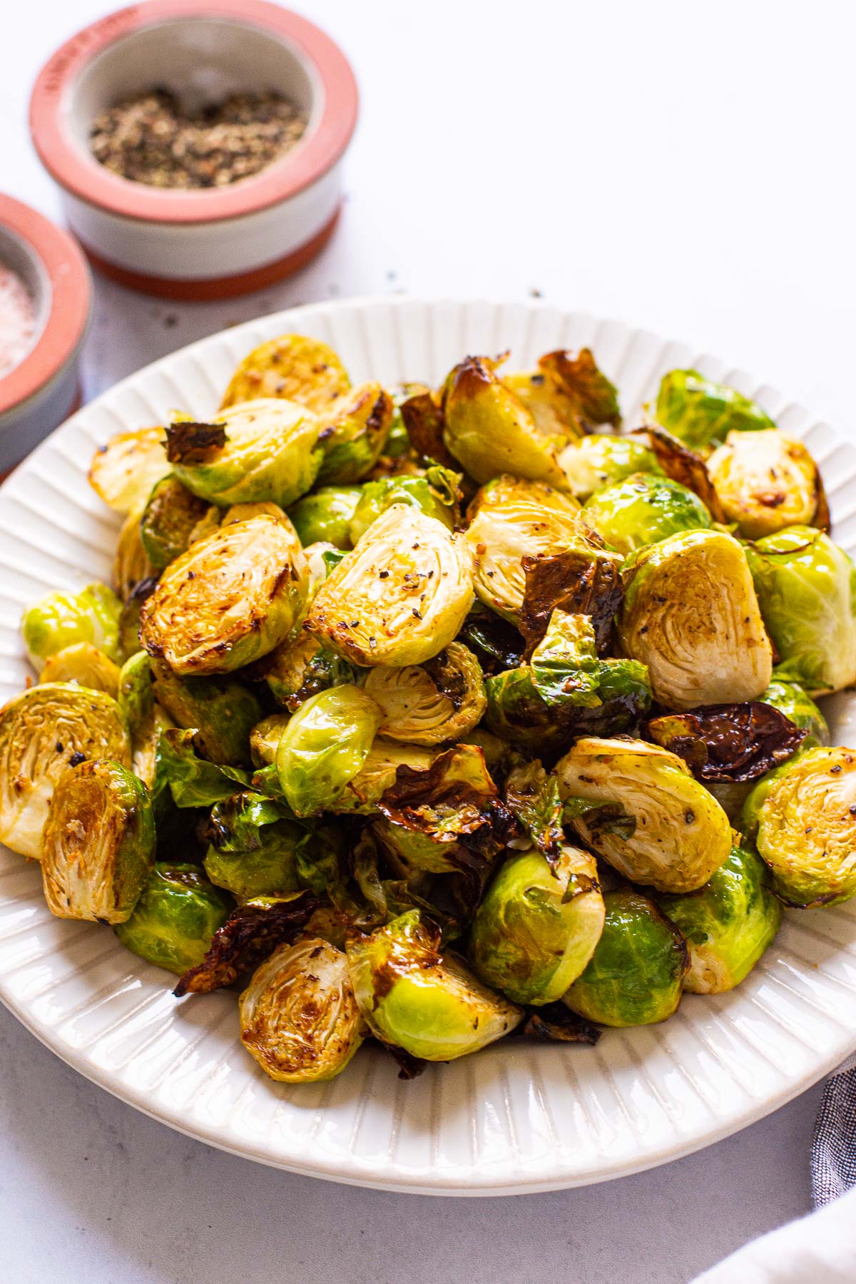 Air fryer brussels sprouts on a plate with salt and pepper in bowls nearby.