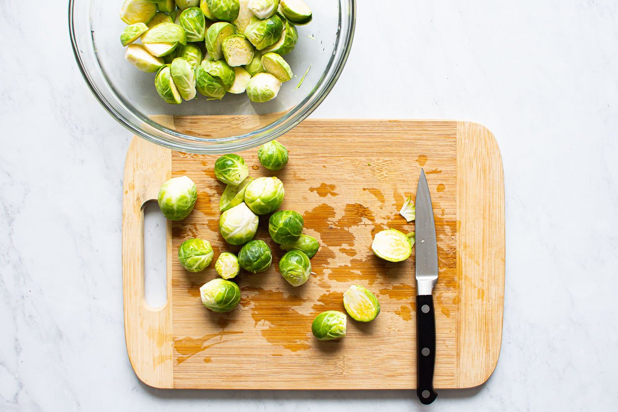 Trim and cut in halves brussels sprouts on a cutting board.