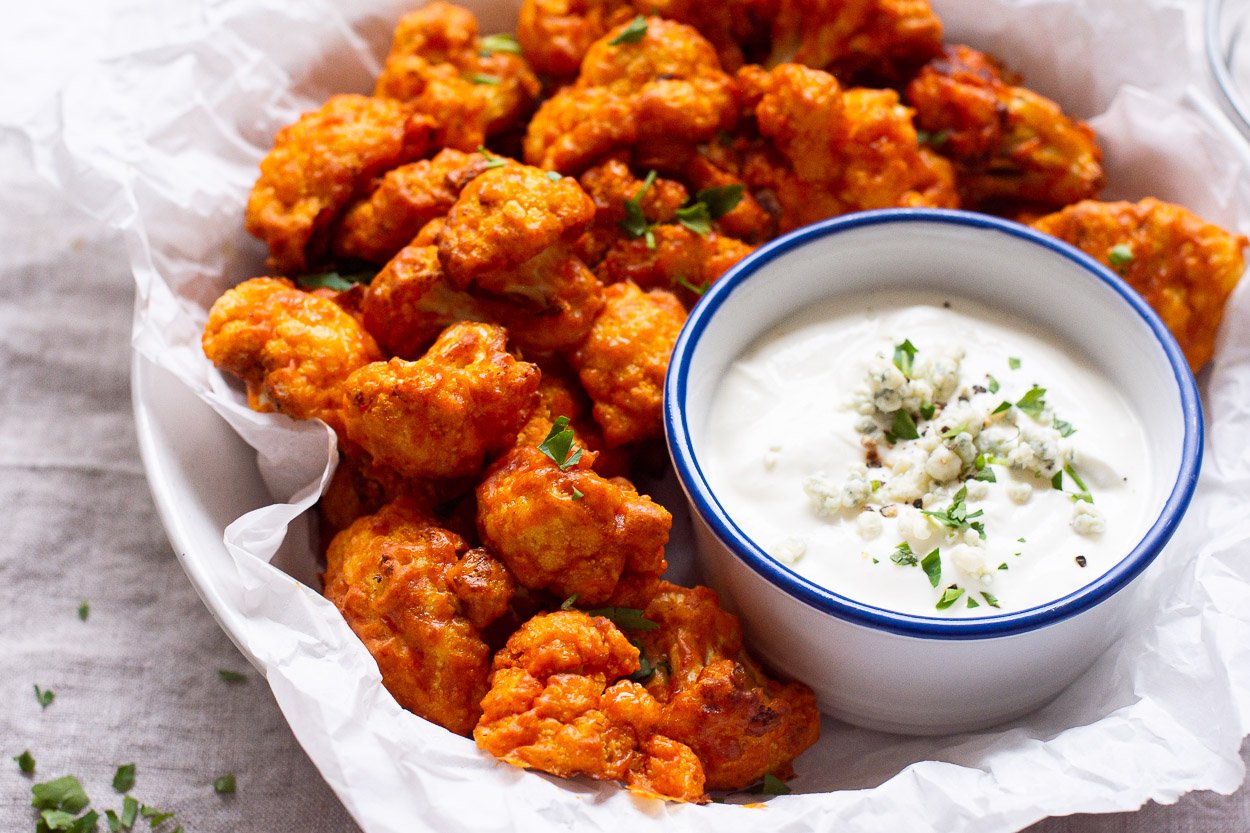 Air fryer buffalo cauliflower garnished with parsley and served with blue cheese yogurt dip.